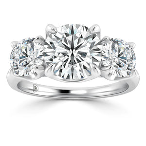 A platinum ring featuring three round brilliant-cut diamonds, with a large center stone flanked by two slightly smaller diamonds, all set in a polished, sleek band.