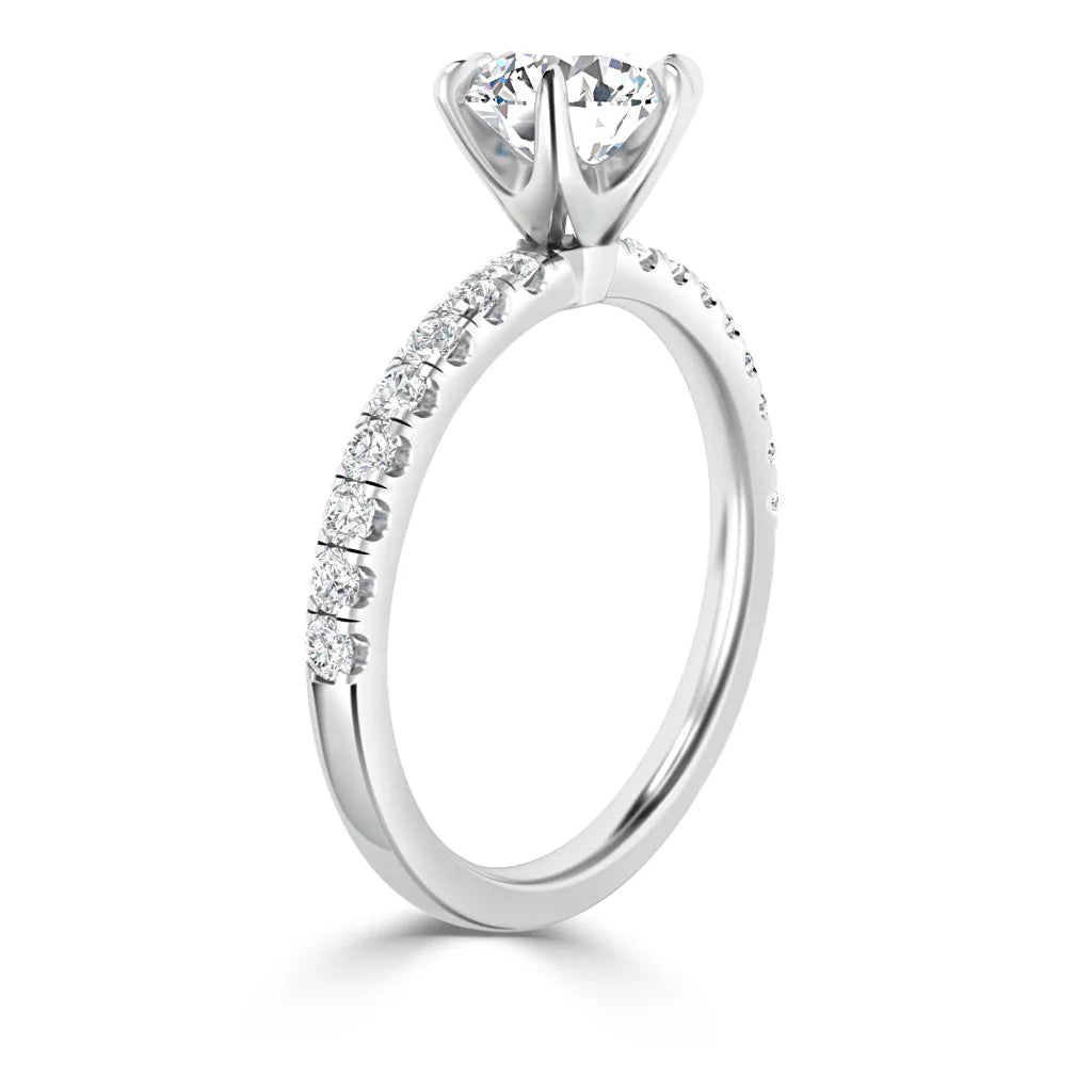 A silver engagement ring with a round solitaire diamond and smaller diamonds set along the band.