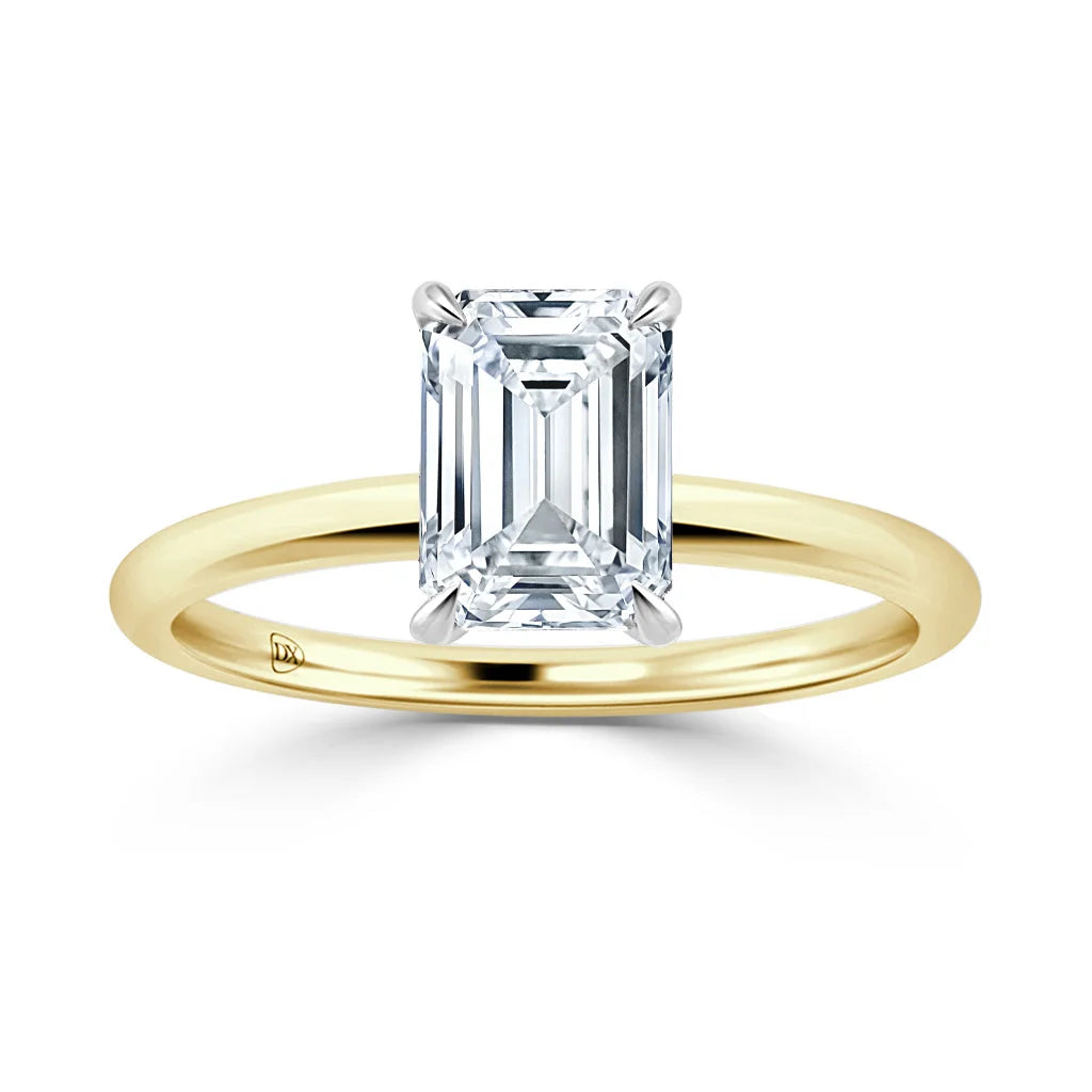 Gold band ring with an emerald-cut diamond solitaire set in four prongs against a white background.